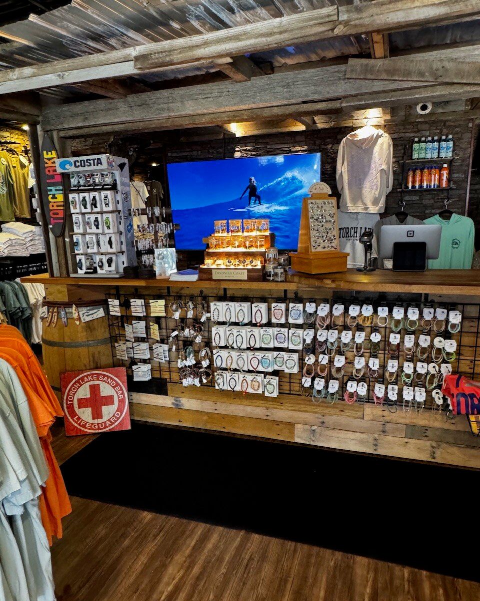 The checkout counter at Torch Lake Surf Co., surf footage playing above it