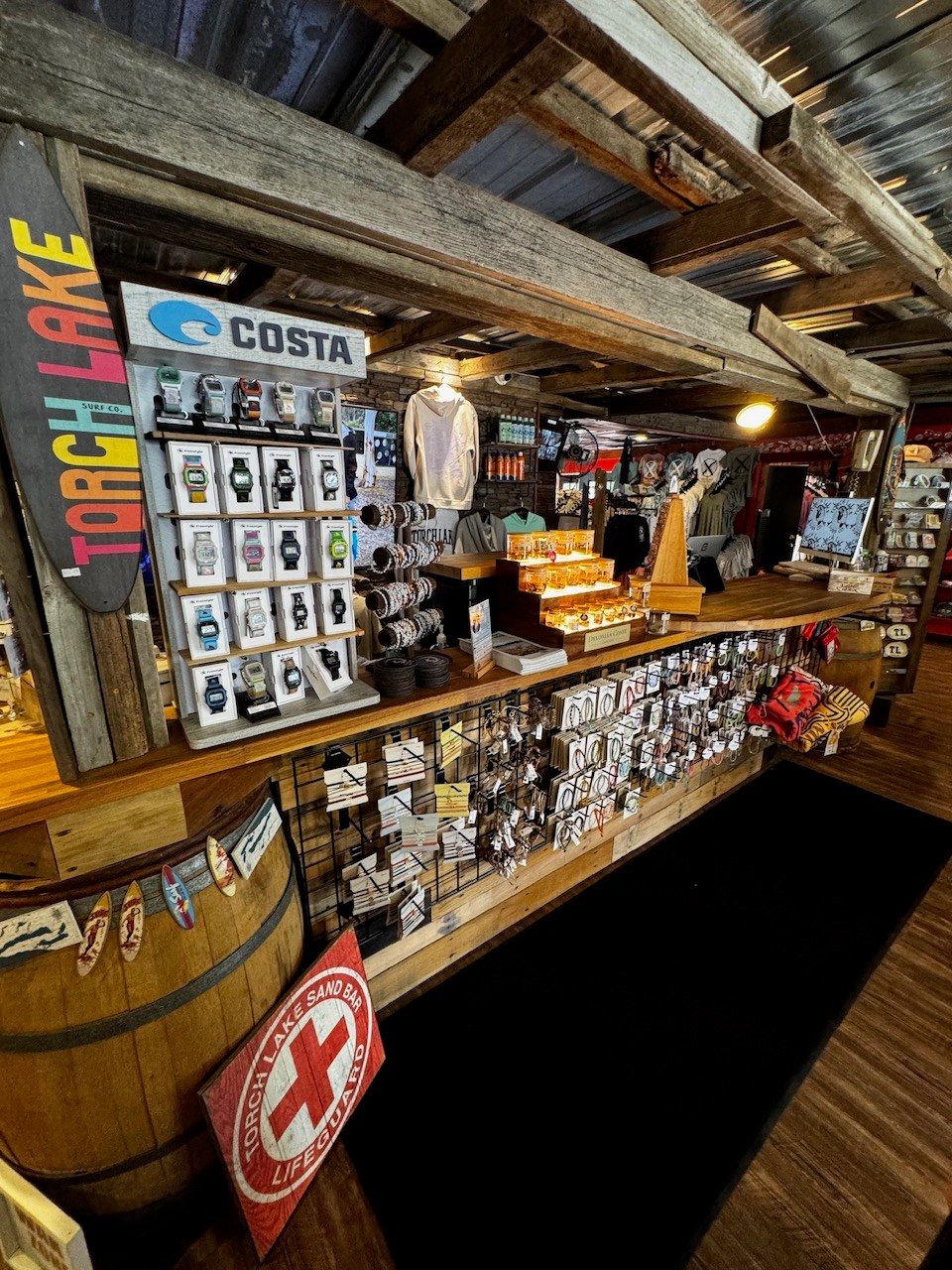 The shop counter with a Costa watch board and a Torch Lake Sand Bar Lifeguard sign