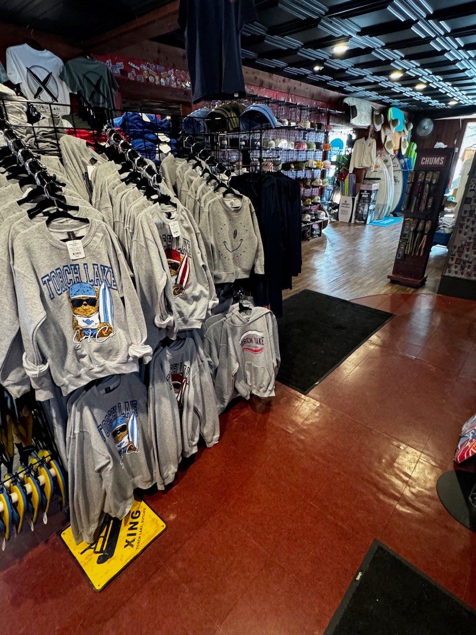 Racks of heather-grey Torch Lake crewnecks and hoodies, with the cap wall and a Chums display further down the floor