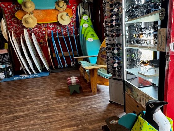 Paddleboards and water skis racked against a red sticker wall, paddles standing alongside