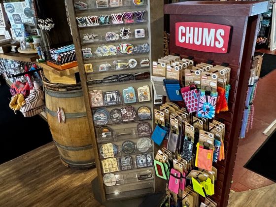 A tall wooden spinner of stickers and patches beside a Chums display of retainers and wallets