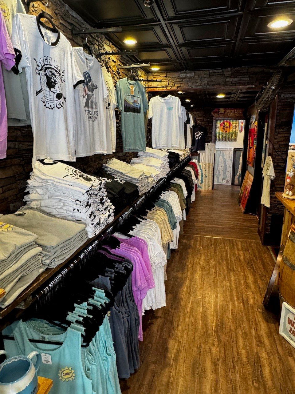 Graphic tees hung and folded along the wall, leading into a hallway of framed Torch Lake map prints