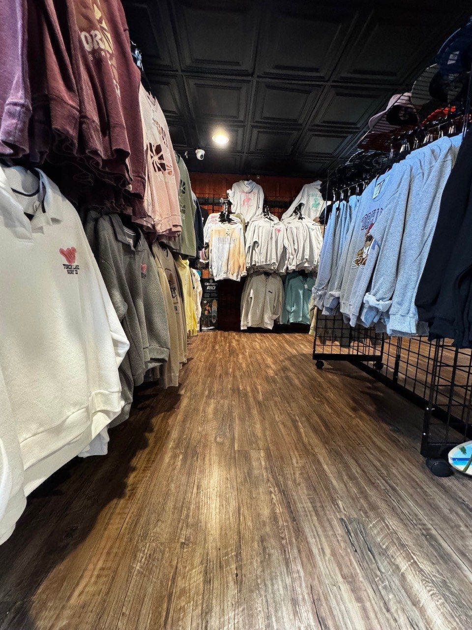 A narrow aisle of hanging sweatshirts and tees in cream, plum, sage and grey on both sides