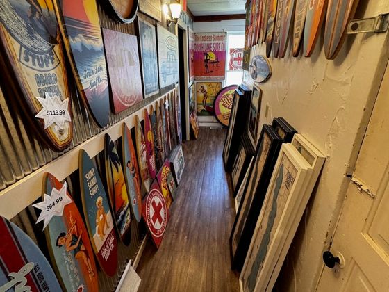 A narrow hallway lined with retro wooden surfboard signs, framed Torch Lake map prints stacked opposite