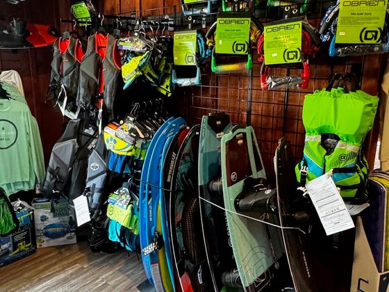 A pegboard wall hung with O’Brien surf ropes and handles above life vests and wakeboards