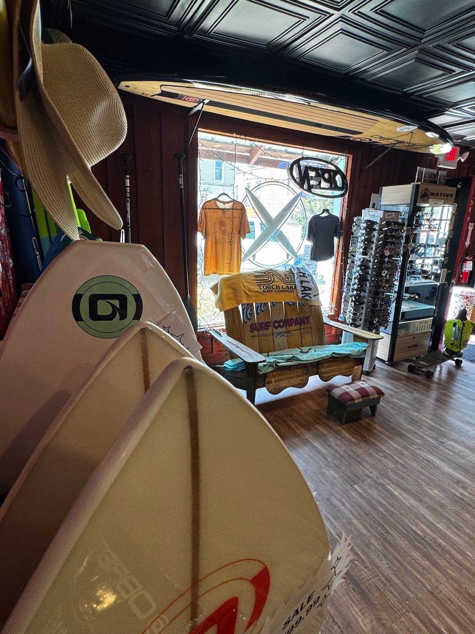 A bench under the front window with an OPEN sign, paddleboards and a surfboard in the foreground